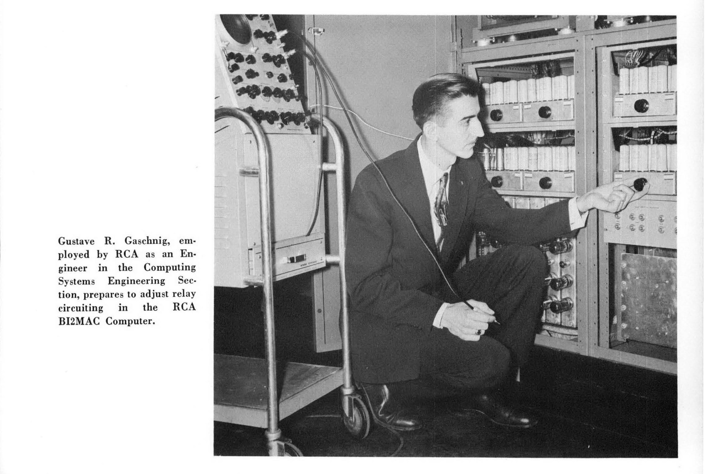 A man kneels beside a computer from the 1950s